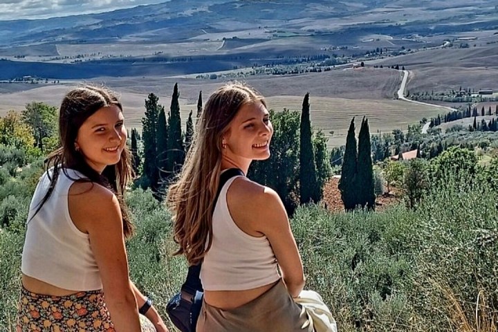 Two women sitting on a ledge overlooking a scenic landscape with hills and trees.