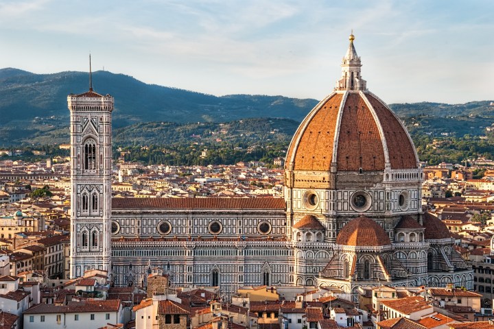 Panoramic view of Florence Cathedral with its iconic dome and bell tower against a mountainous backdrop.