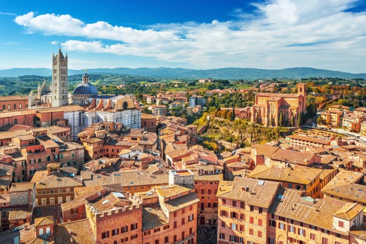 Aerial view of Siena, Italy, with historic buildings and a cathedral under a blue sky.