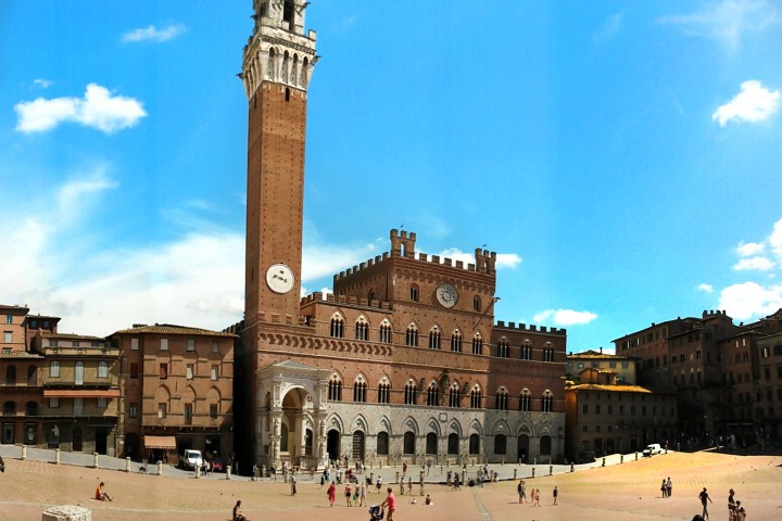 Historic building with tower and clock in a sunny plaza with scattered people.