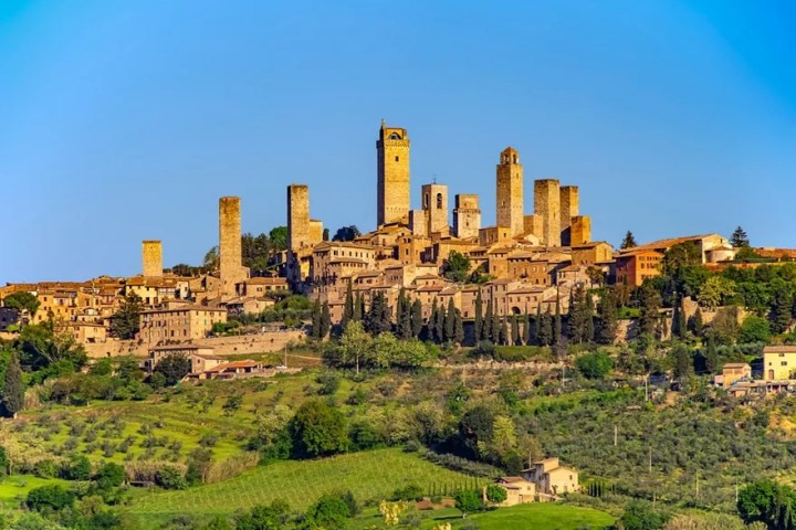 Scenic view of medieval town with tall stone towers and green landscape under a clear blue sky.