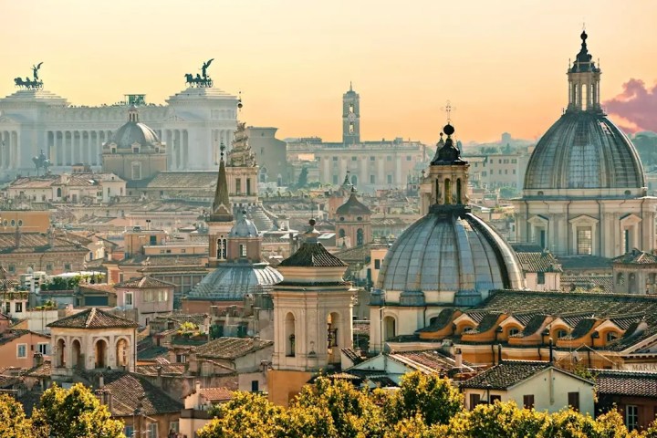 Scenic view of Rome's historic skyline with domes and ancient buildings at sunset.