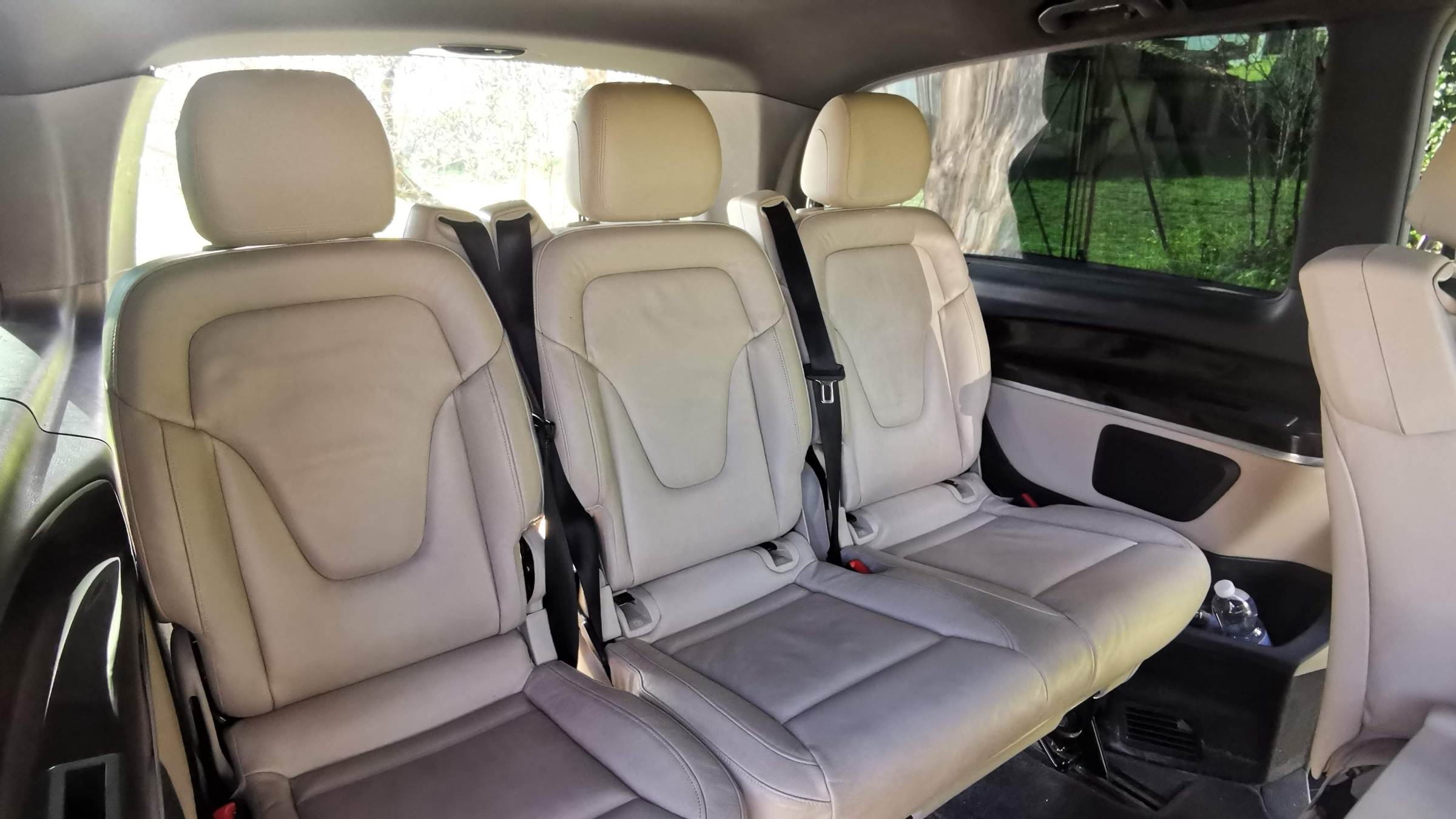 Interior view of a car's back seats, showing beige leather and seatbelts.