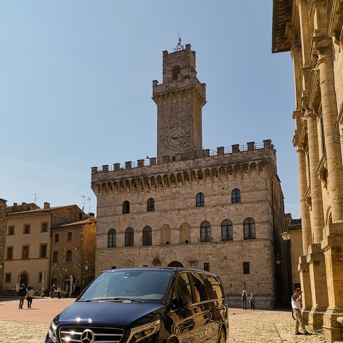 Black van parked in front of historic stone building with clock tower.